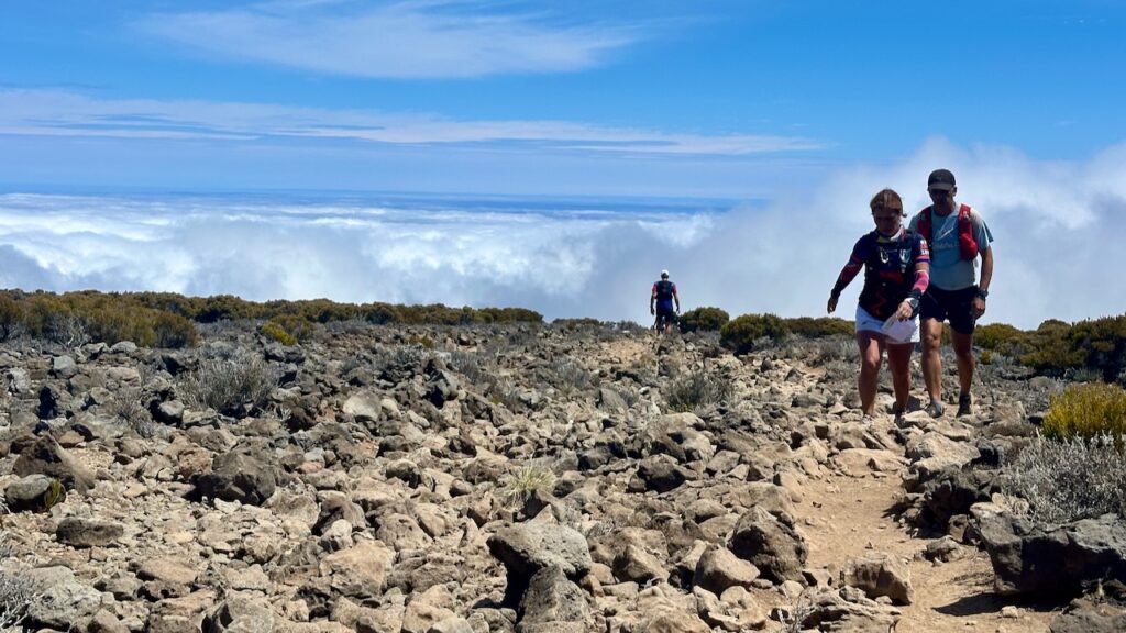 Traileurs progressant sur le terrain volcanique du Grand Bénare au-dessus de la mer de nuages